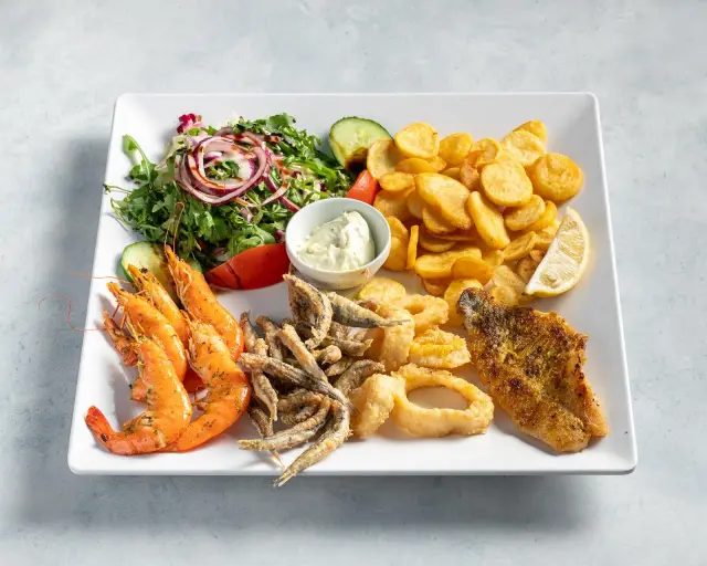 Teller mit Garnelen, Sardellen, Calamari-Ringen und Fischfilet, dazu Kartoffelchips, Salat und Knoblauchdip